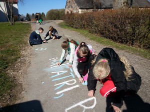 Ar krītiņiem skolēni raksta literatūras citātus uz asfalta